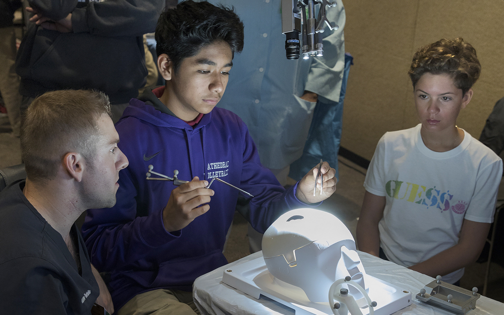 Two teen boys performing a simulation brain surgery with a doctor.