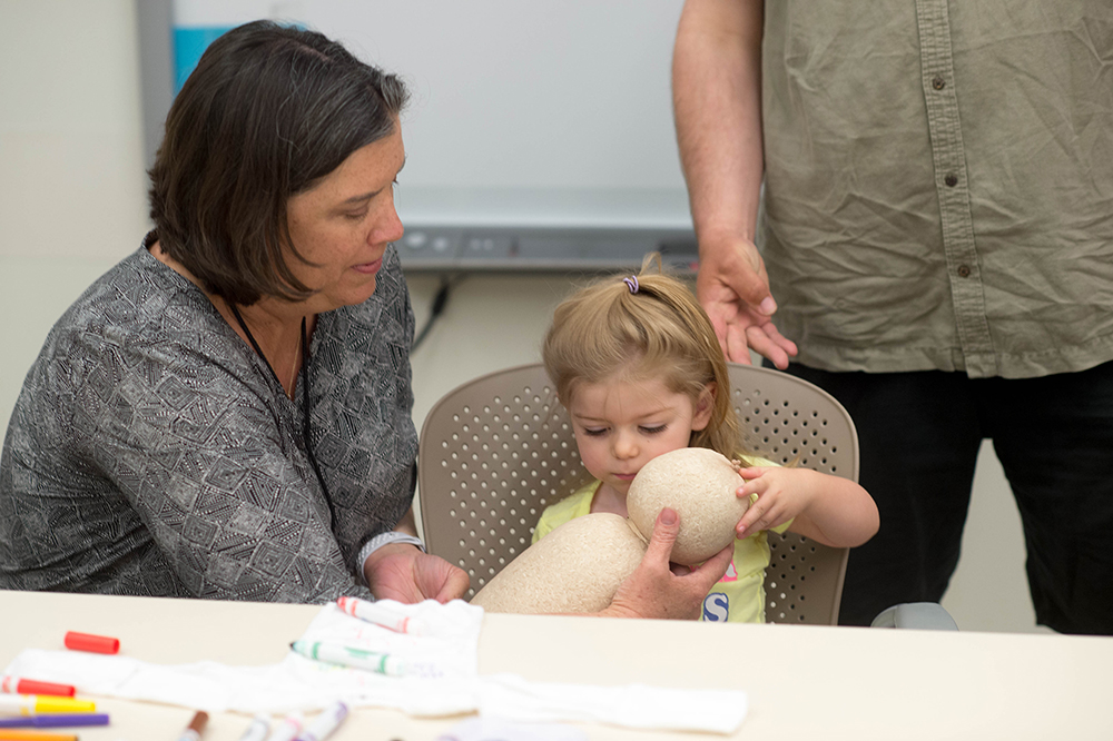 Cedars-Sinai social worker Randie Cloutier-Chaine shows 2-year-old Meredith Shafer how to properly hold her baby sister using a doll.