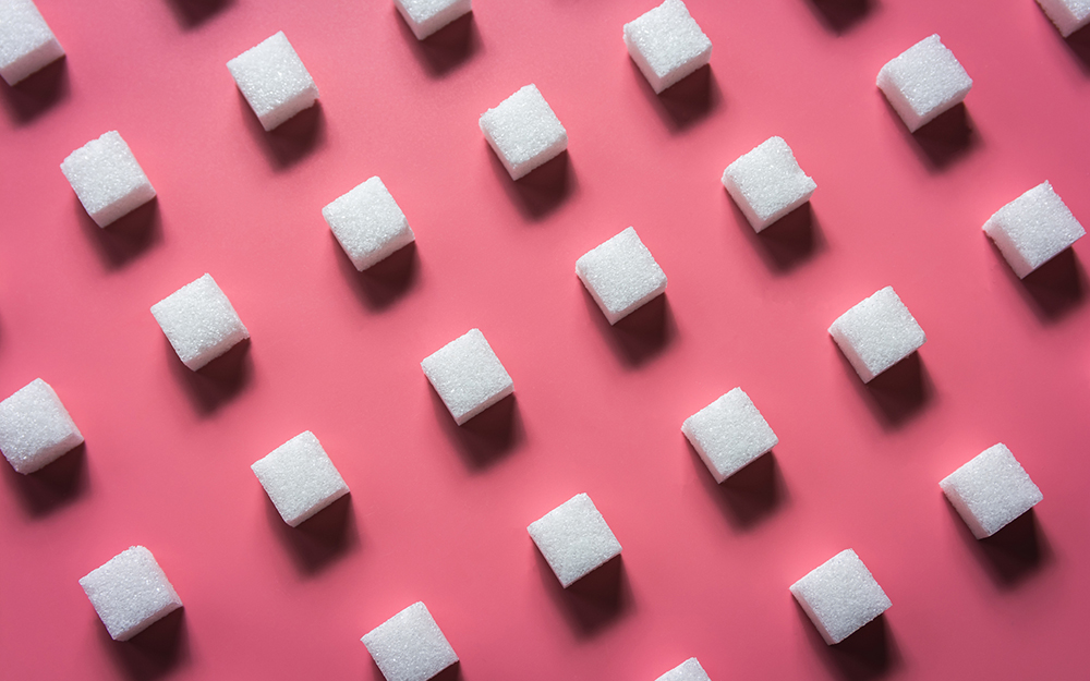 Sugar cubes lined up on a pink table.
