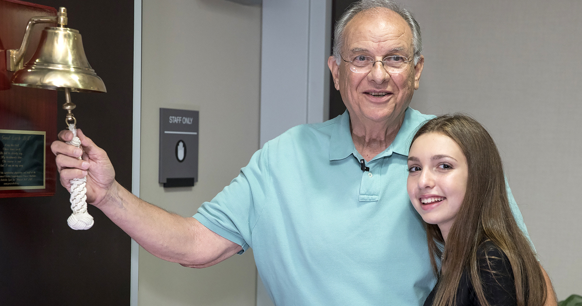 Art Tostado and Isabella Spar are shown with a newly installed ceremonial bell at Cedars-Sinai that signals the end of treatment.