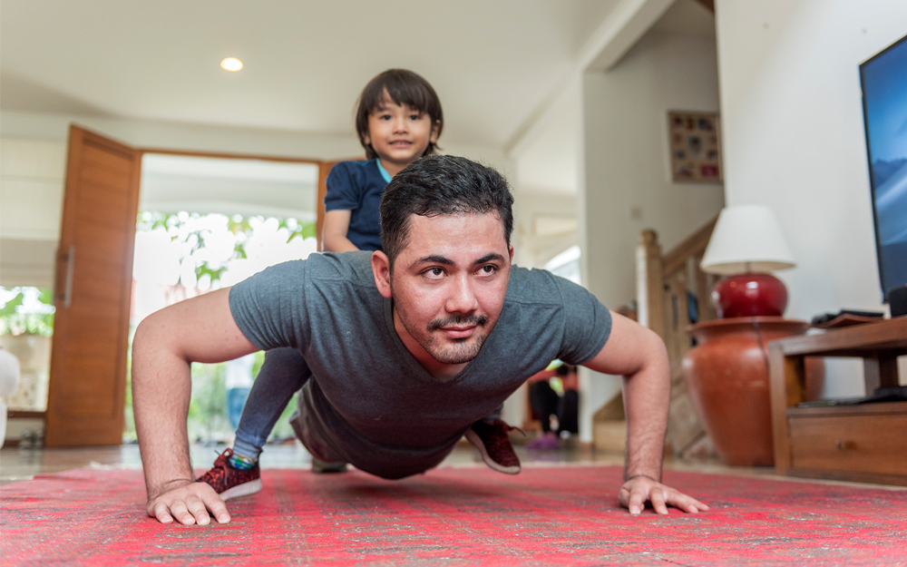 Man doing a push-up with a child sitting on his back.